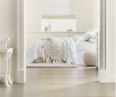 Entryway view into monochromatic neutral bedroom with crocheted throw and round pouf.