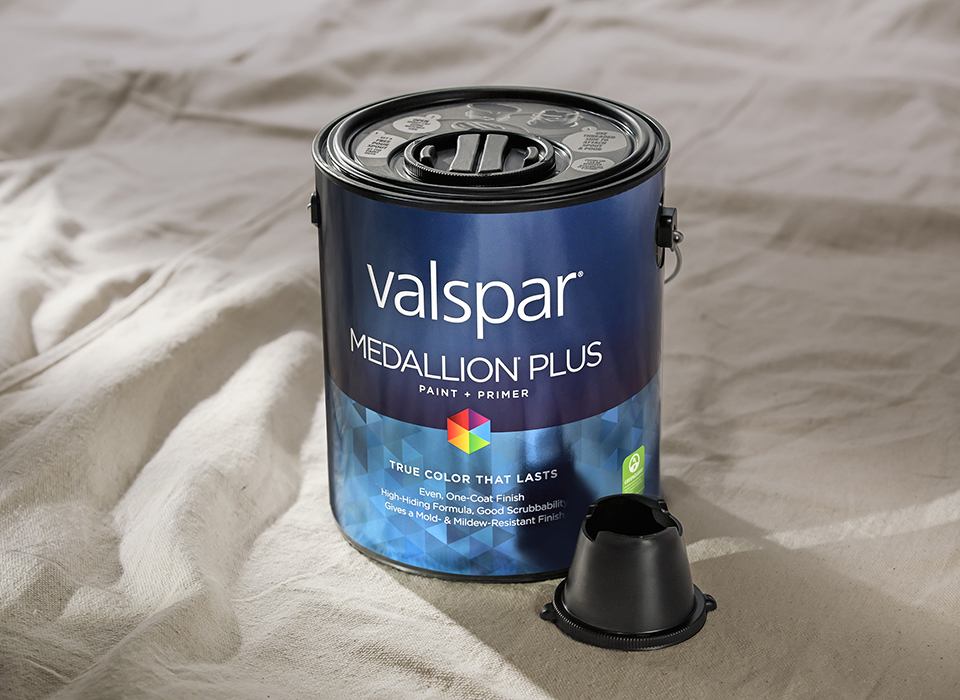 Gloved hand with brush applying stain to wood railing.