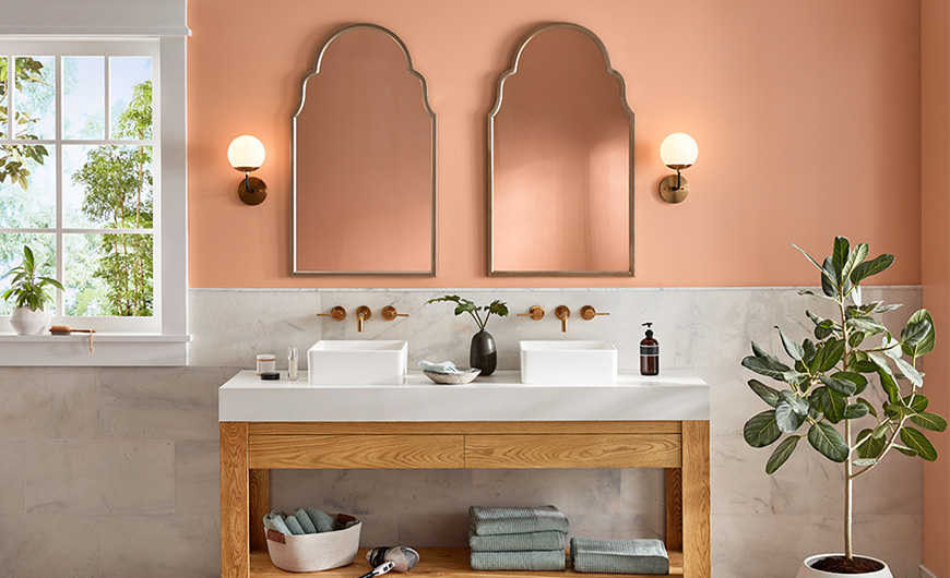 Straight-on view of double sink with copper fixtures against a sand-colored wall with double mirrors.