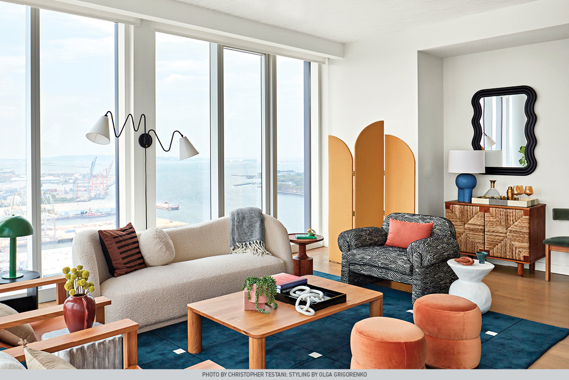 White walls frame floor-to-ceiling windows overlooking NYC. Neutral furniture and accessories with tall room divider.