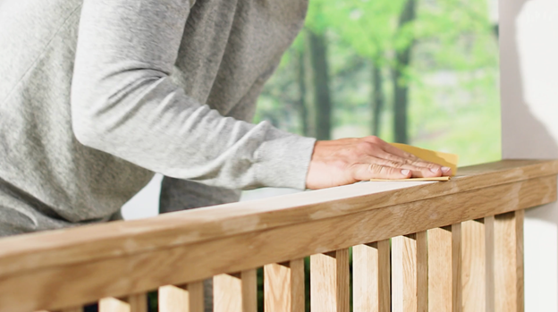Hand with sander prepping top of wood railing.