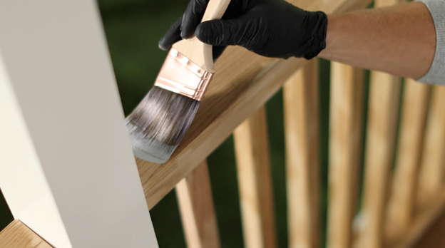 Gloved hand using brush to stain top of railing.
