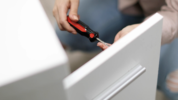 Open white vanity door with hand holding screwdriver to loosen screws and remove doors.